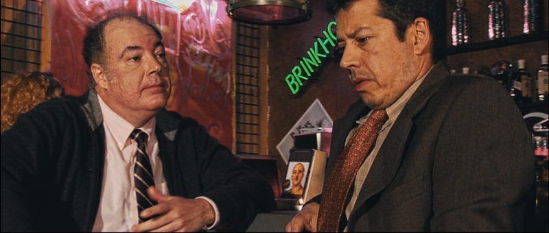 Escena de la película "Soñando en 35 mm." en un bar, con dos personajes en conversación.
