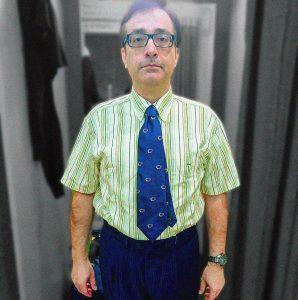 Hombre con gafas, camisa a rayas y corbata en un ambiente de oficina o estudio.