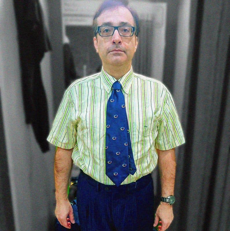 Hombre con gafas, camisa a rayas y corbata en un ambiente de oficina o estudio.